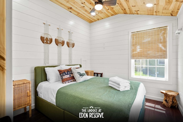 Una habitación con cama, ventana con persianas, ventilador de techo y decoración en la pared.