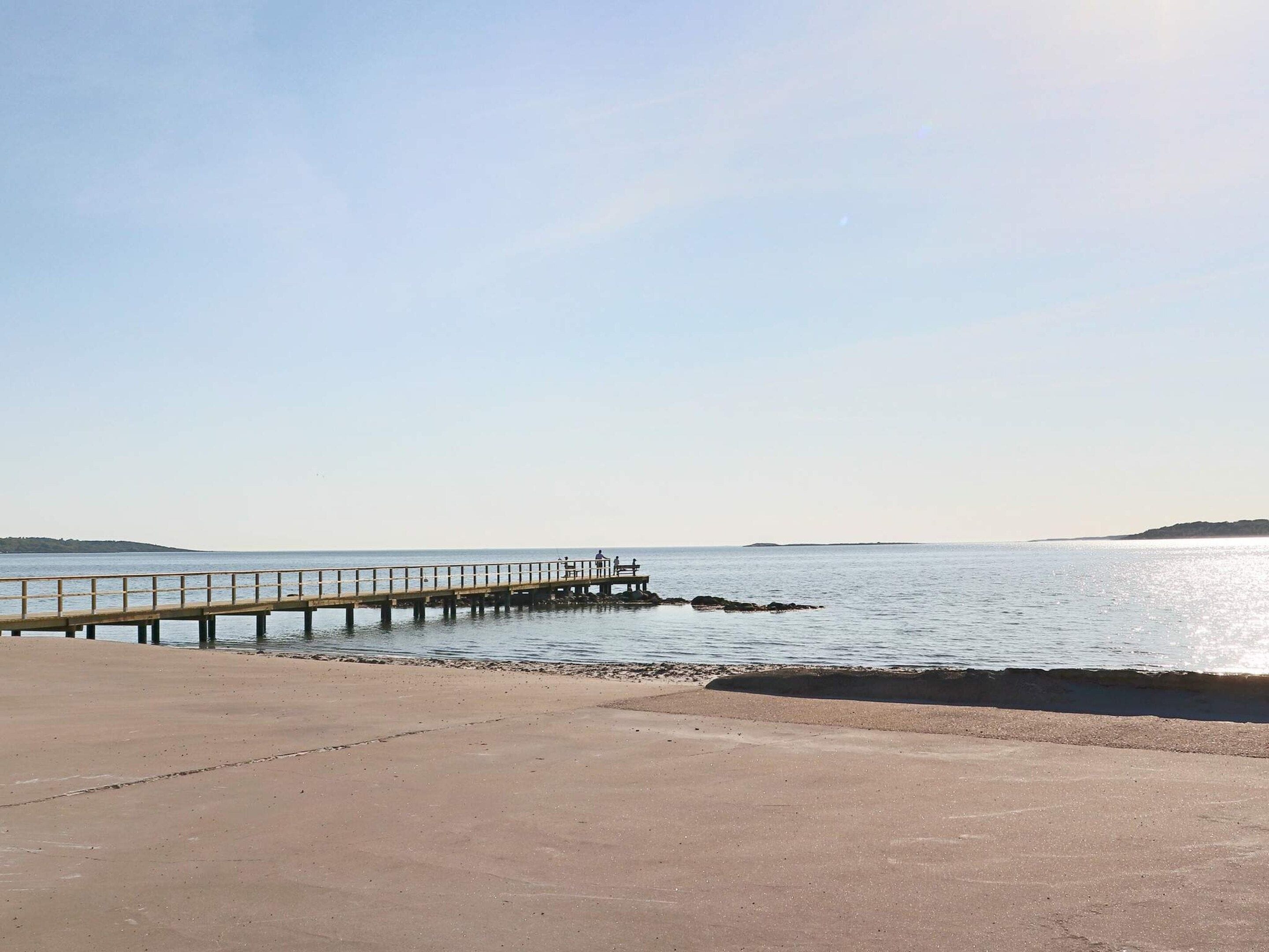 A concrete walkway leading to a pier extending into calm water, with a distant landmass visible.