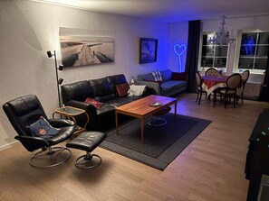 A modern living room with a black leather sofa, a wooden coffee table, a black leather chair, and a dining area with a table and chairs. - 4 Star Holiday Home in Frillesas (Frillesas)