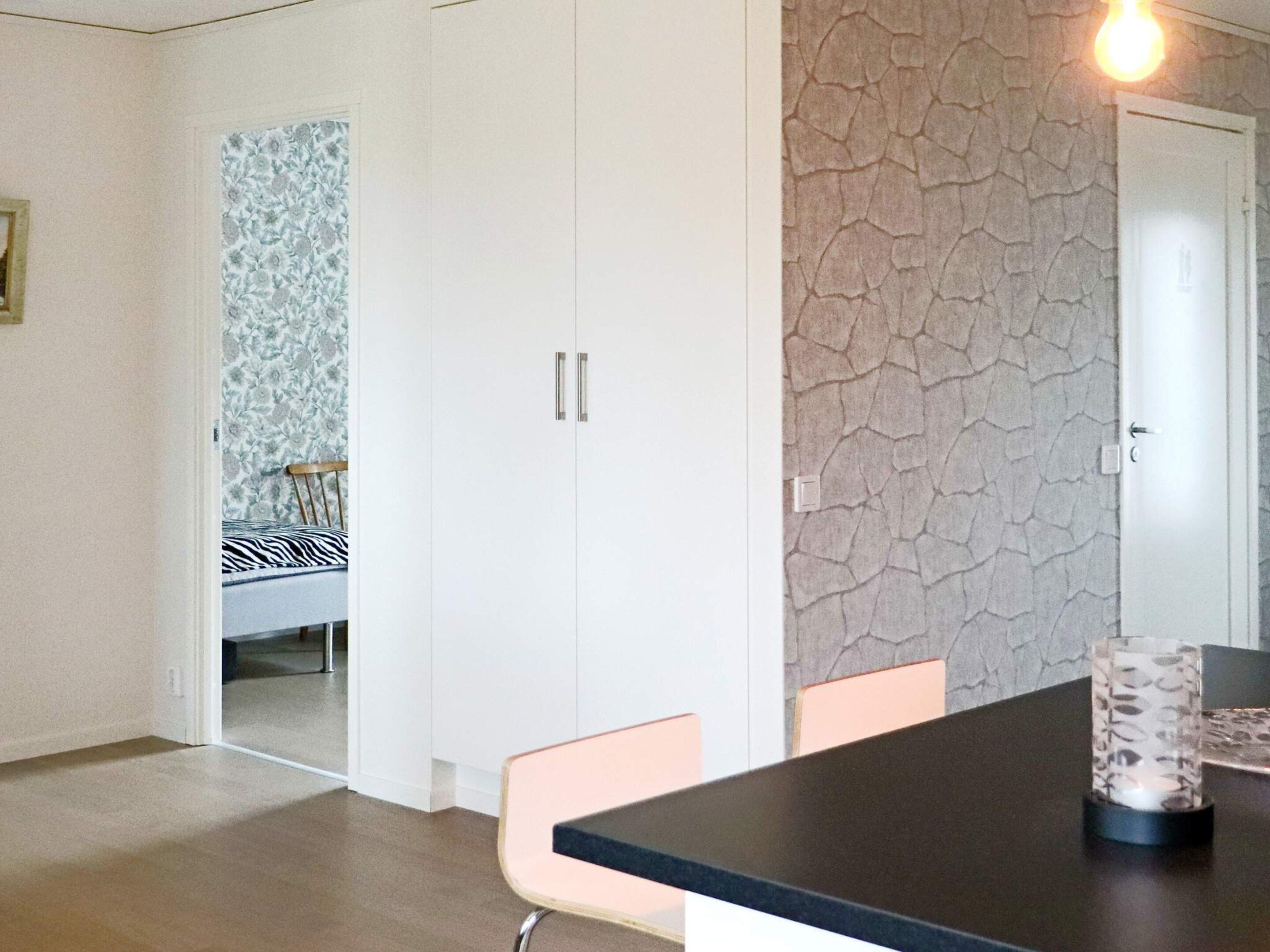 A room with a dining table, chairs, a wardrobe, and a patterned wallpaper.