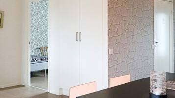 A room with a dining table, chairs, a wardrobe, and a patterned wallpaper.