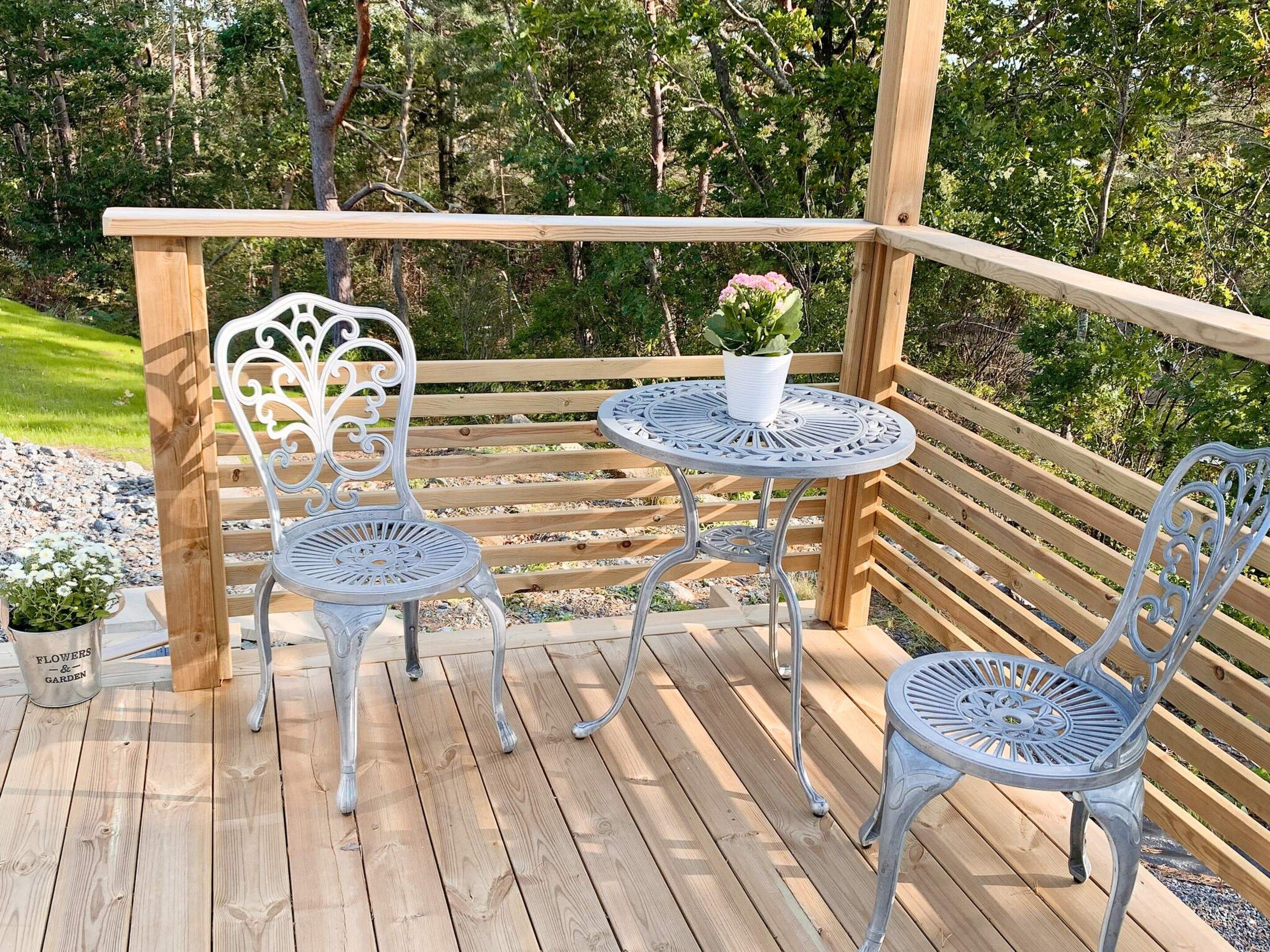 A wooden deck with two metal chairs and a small round table, surrounded by a wooden railing.