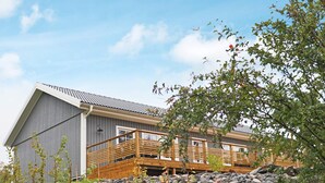 A modern building with a wooden deck, stone wall, and a clear sky. - 4 Star Holiday Home in Frillesas (Frillesas)