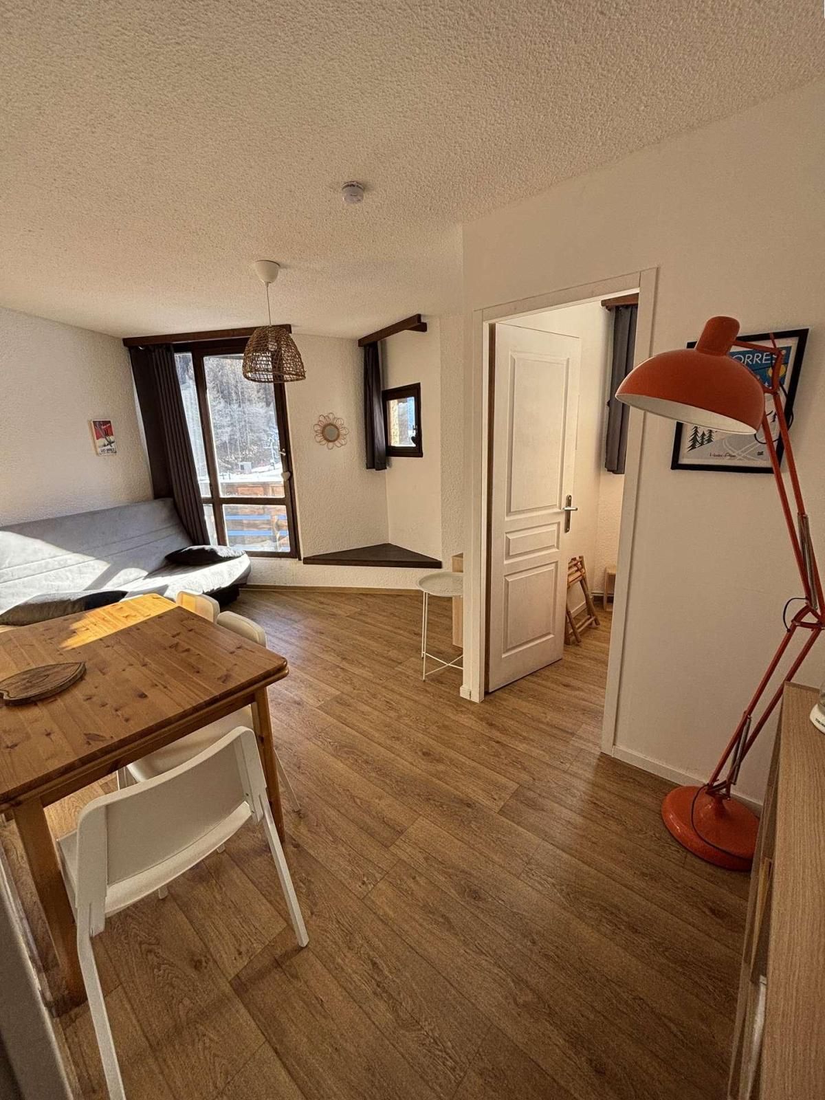 Une pièce comprenant une table à manger en bois, une chaise blanche, un lampadaire rouge et une porte donnant sur une autre pièce.