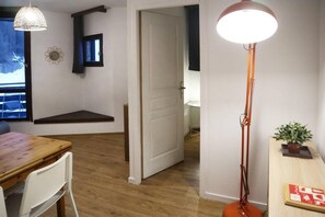 Een kamer met houten vloer, een eettafel met stoelen, een grote vloerlamp en een kleine tafel met een plant.