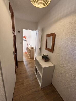 A hallway with a wooden floor, a white console table with a plant, a mirror, and a door leading to a room with a bed and a window. - 15m from ski slopes, 6th floor, view ski slopes, balcony, tv, ski locker, 33m², Les Orres (Les Orres)