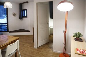 A room with a wooden floor, a dining table with chairs, a pendant light, a floor lamp, a small table with a plant, and a door leading to another room. - 15m from ski slopes, 6th floor, view ski slopes, balcony, tv, ski locker, 33m², Les Orres (Les Orres)