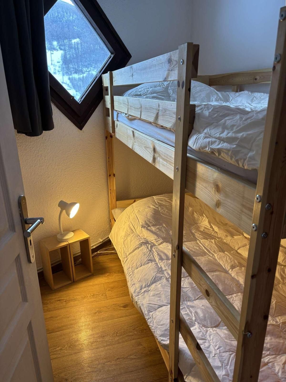 A small, cozy room with a bunk bed, a desk with a lamp, and a window overlooking a snowy landscape.