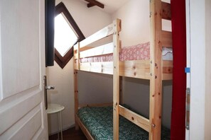 A small room with a bunk bed, a small table, and a window.