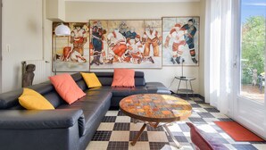A living room with a black leather sofa, colorful cushions, a patterned coffee table, and large sports-themed paintings on the wall.