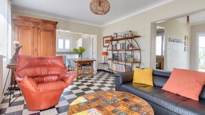 A living room with a checkered floor, a leather armchair, a sofa with cushions, a coffee table, a bookshelf, and a dining area with chairs and a table.