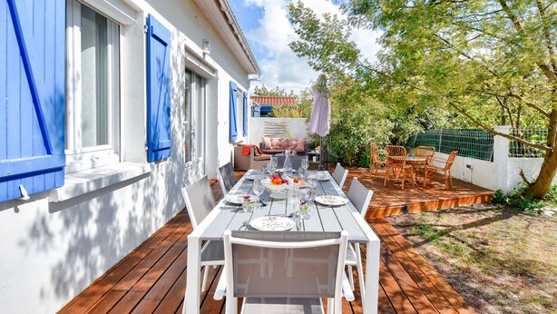 An outdoor dining area with a wooden deck, white walls, and blue shutters.