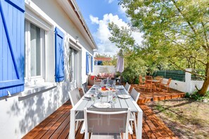 An outdoor dining area with a wooden deck, white walls, and blue shutters.