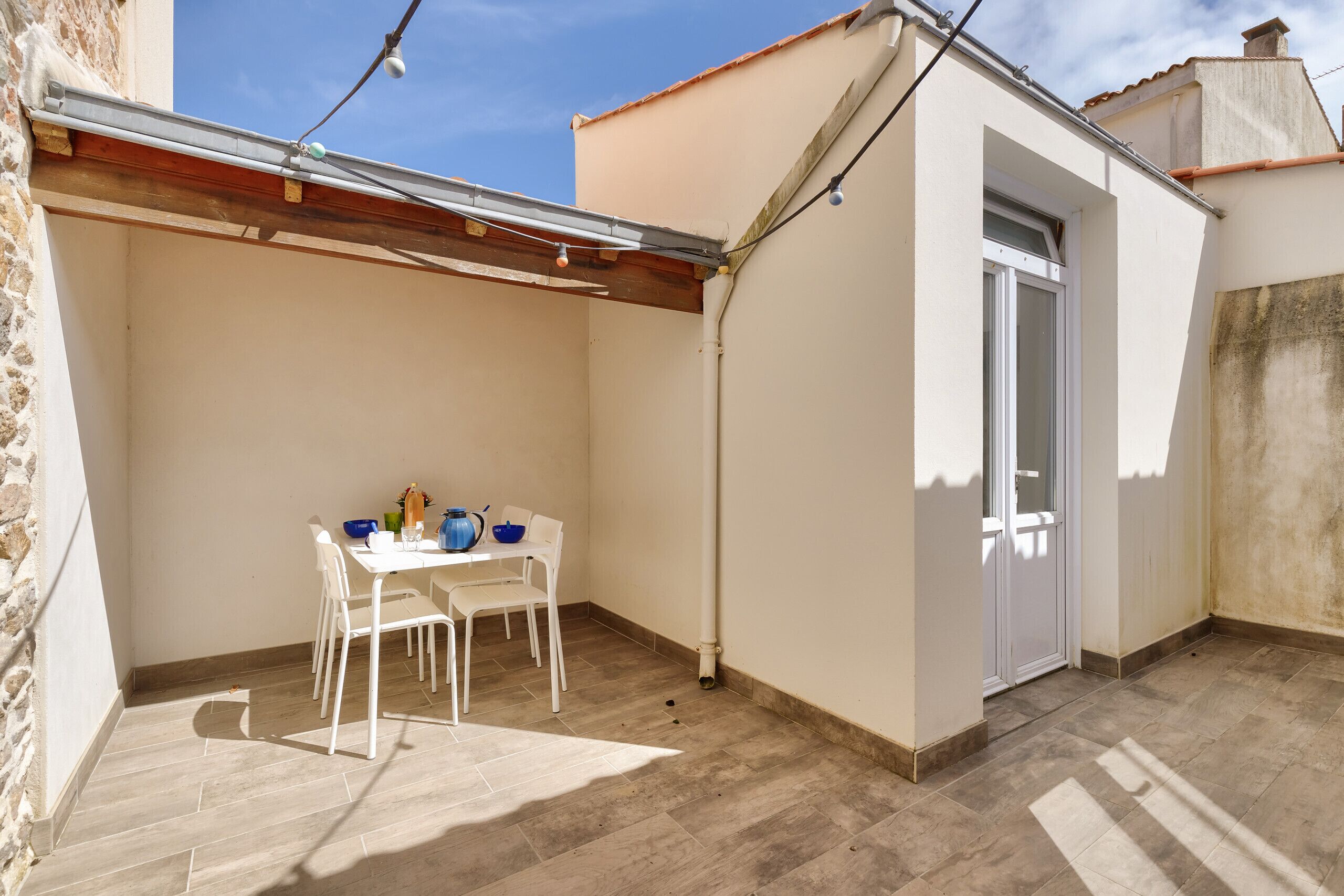 Ein kleiner, abgeschlossener Patio-Bereich mit Tisch, Stühlen, einer Tür und einem Fliesenboden.