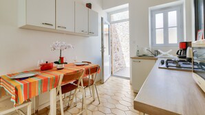 A dining area with a table set for two, a vase of flowers, and a window with a view of a stone wall. - Getaway 150m from the beach in Les Sables d'Olonne (Les Sables-d´Olonne)