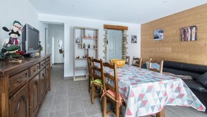 Ein Essbereich mit einem Tisch für vier Personen, Holzsesseln, einer Holzsideboard und einem Fernseher auf einem Schrank.