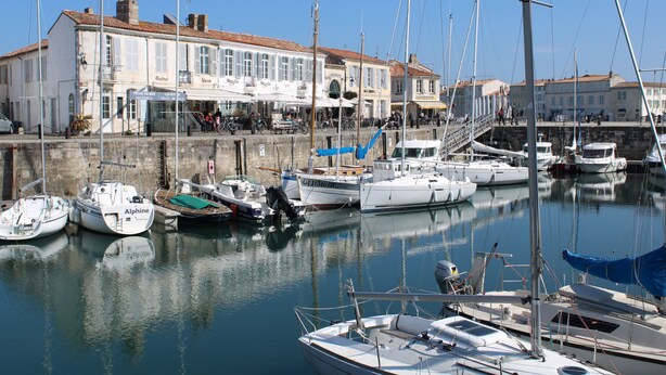 Un port de plaisance avec des bateaux amarrés, un bâtiment doté d’un toit en tuiles et un mur en pierre.
