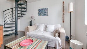 Une pièce moderne avec un escalier en colimaçon, un canapé blanc, une table à rayures colorées et un tableau abstrait bleu.