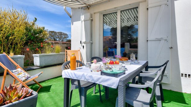 Eine Terrasse mit Esstisch und Stühlen, umgeben von einem überdachten Bereich mit gestreifter Markise.
