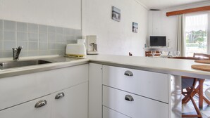 Eine moderne Küche mit Spüle, weißen Schränken und einer Kaffeemaschine. Es gibt einen Essbereich mit Tisch und Stühlen.