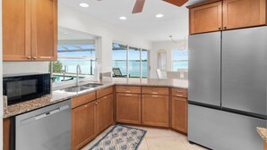 A modern kitchen with wooden cabinets, stainless steel appliances, a ceiling fan, and a view of the ocean. - Waterfront 3/3 Home with Panoramic Bay Views! (Marco Island)