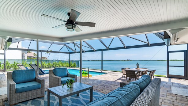 A covered outdoor area with wicker furniture, a pool, and a view of the ocean. - Waterfront 3/3 Home with Panoramic Bay Views! (Marco Island)