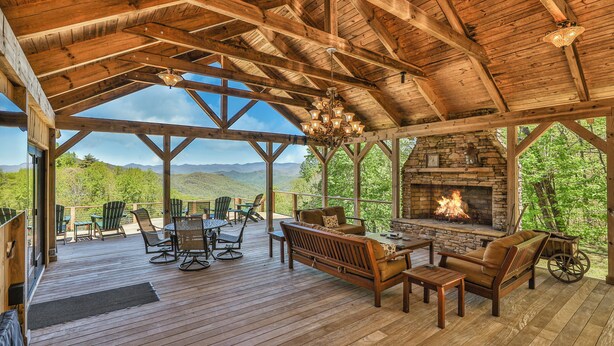 A wooden deck with a stone fireplace, outdoor seating, and a scenic mountain view. - GrandView @ Smoky Ridge: Stunning Mtn Views, Large Deck & Windows | Pet Friendly (Cullowhee)