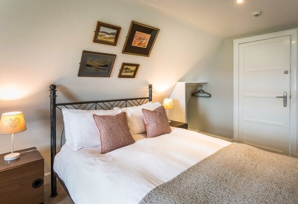 A neatly made bed with white and brown bedding, a bedside lamp, and a wall-mounted picture frame. - Lamlash Bay Hotel (Isle of Arran)