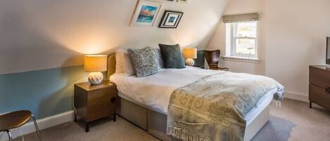 A bedroom with a bed, bedside lamps, a nightstand, a chair, and a window with curtains.