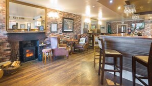 A cozy pub with a brick wall, a fireplace, comfortable seating, and a bar area. - Lamlash Bay Hotel (Isle of Arran)
