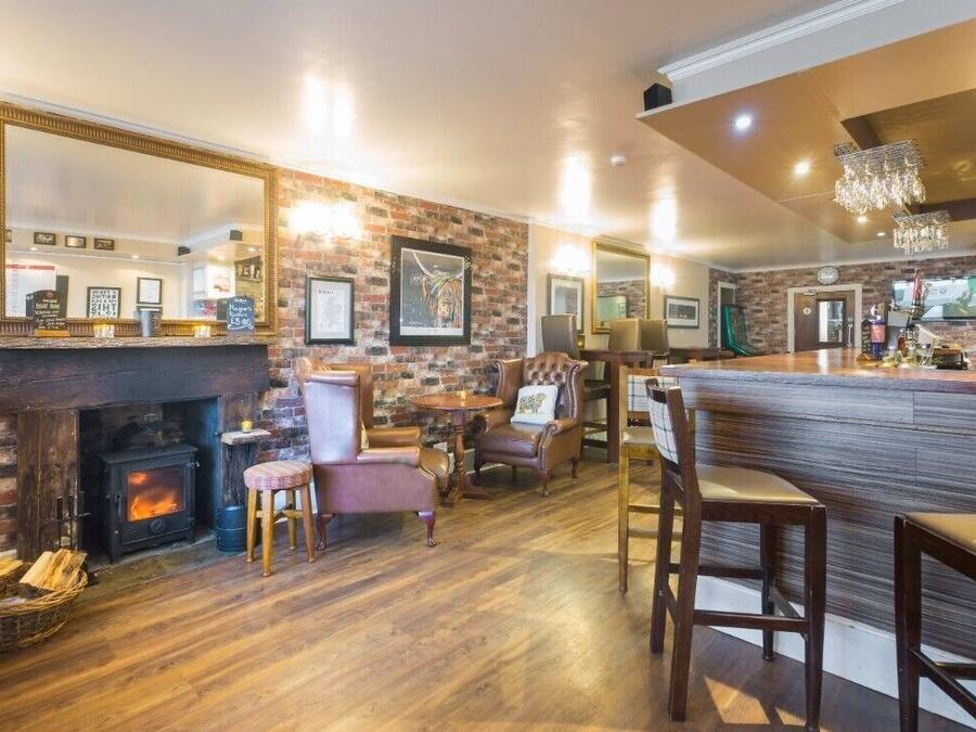 A cozy pub with a brick wall, a fireplace, comfortable seating, and a bar area.