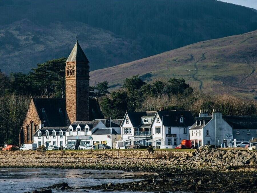 A coastal town with a prominent church tower, white buildings, and a rocky shoreline.