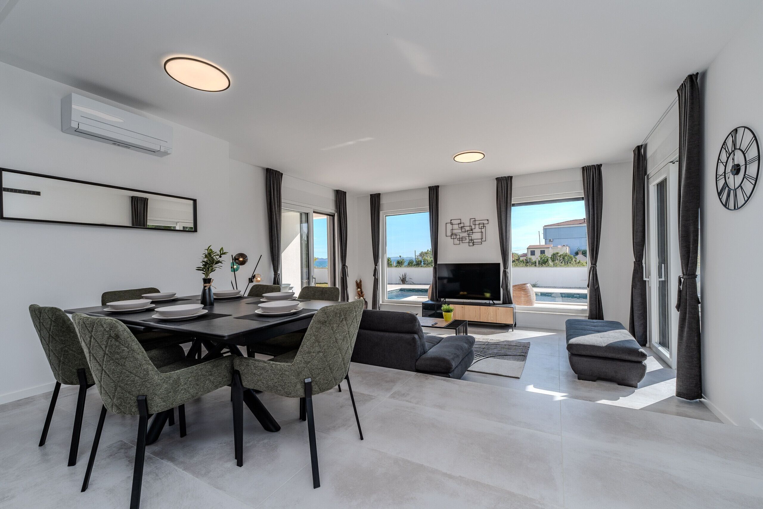 A modern living room with a dining area, large windows, and a flat-screen TV.