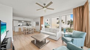 Ein modernes Wohnzimmer mit einer Couch, einem Couchtisch und einem Fernseher. Es gibt einen Essbereich mit Stühlen und eine Küche im Hintergrund.