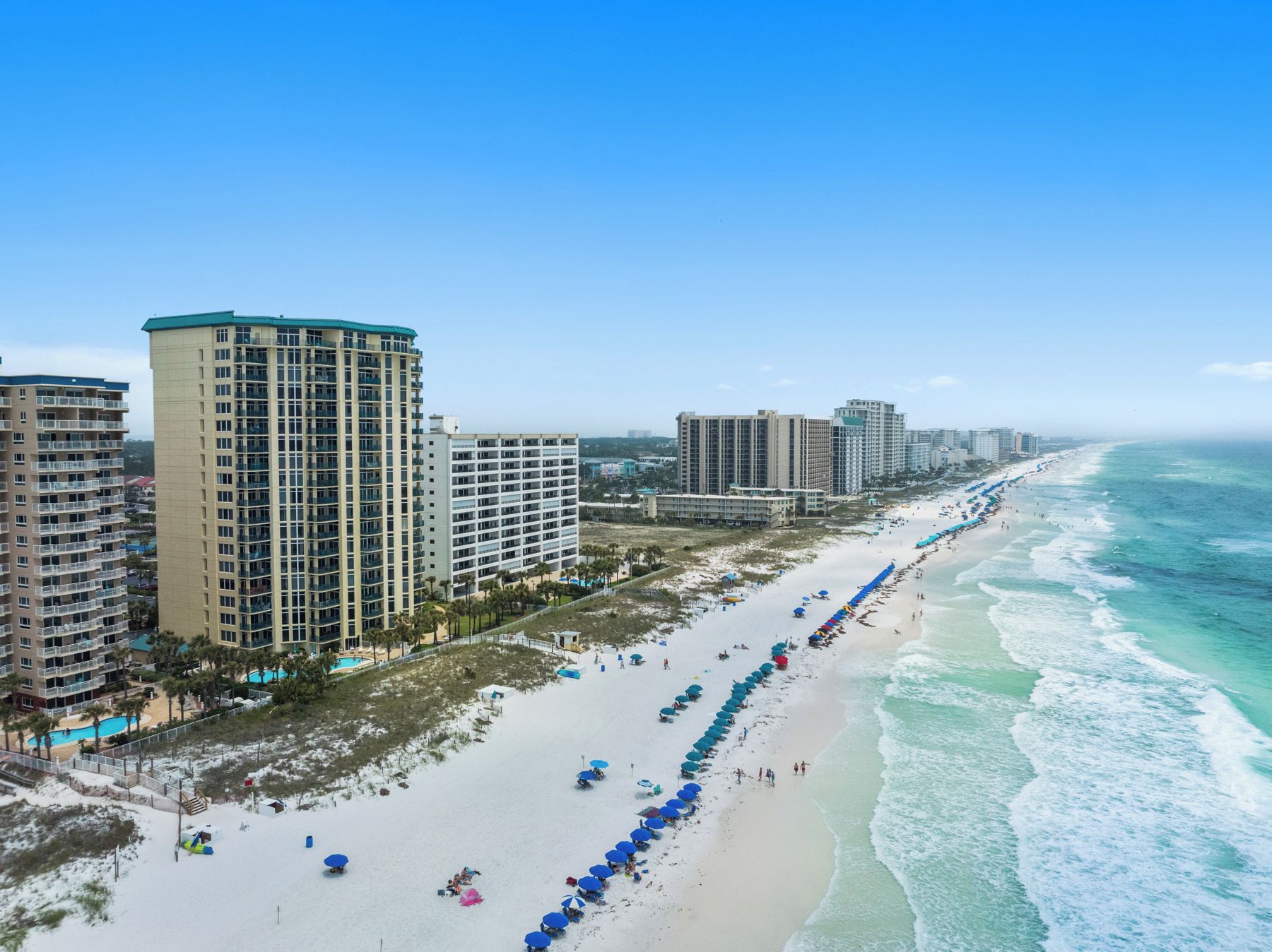 A coastal hotel with multiple high-rise buildings, a sandy beach with umbrellas, and ocean views.