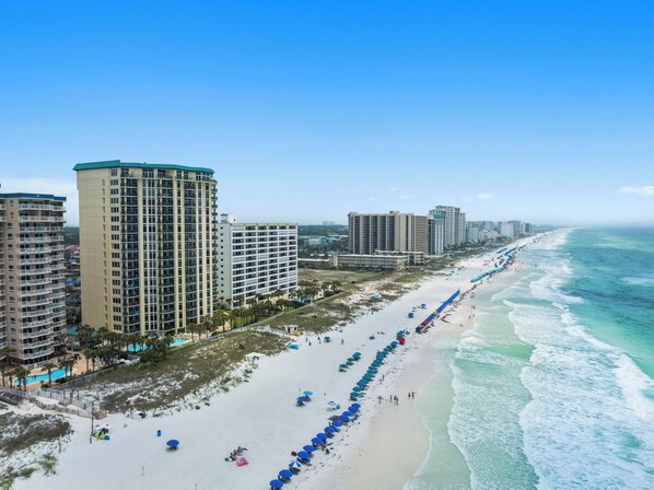 Ein Küstenhotel mit mehreren Hochhäusern, einem Sandstrand mit Sonnenschirmen und Blick auf den Ozean.
