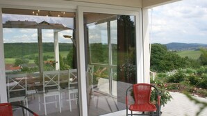 A glass-enclosed patio with a table and chairs, offering a view of a green landscape. - Holiday Home Hornchens Horle (Volkmarsen)