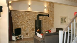 A cozy living room with a stone wall, a fireplace, a sofa, and a TV on a stand. - Holiday Home Hornchens Horle (Volkmarsen)