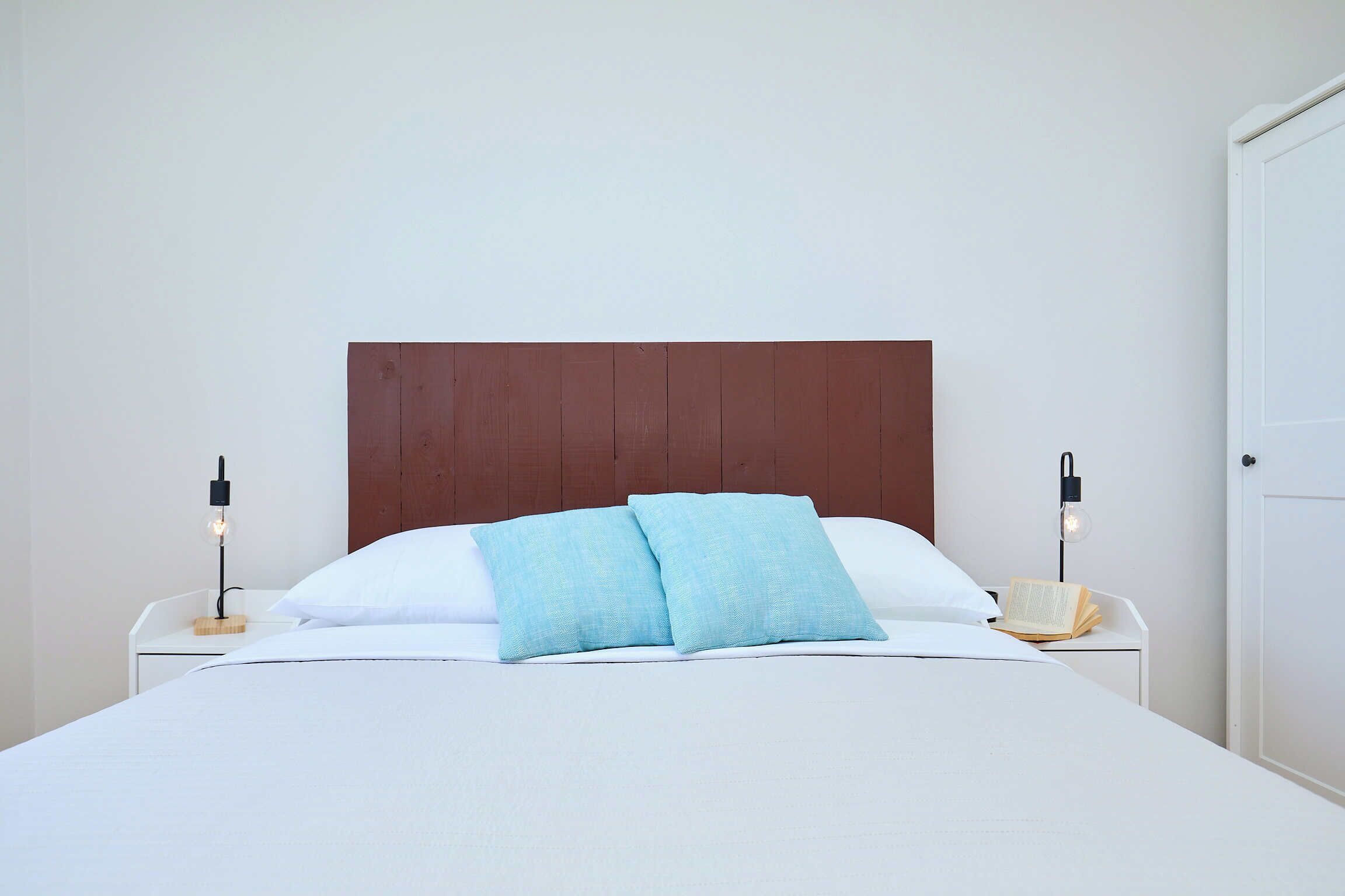 A neatly made bed with a wooden headboard, two bedside tables with lamps, and a closed door in the background.