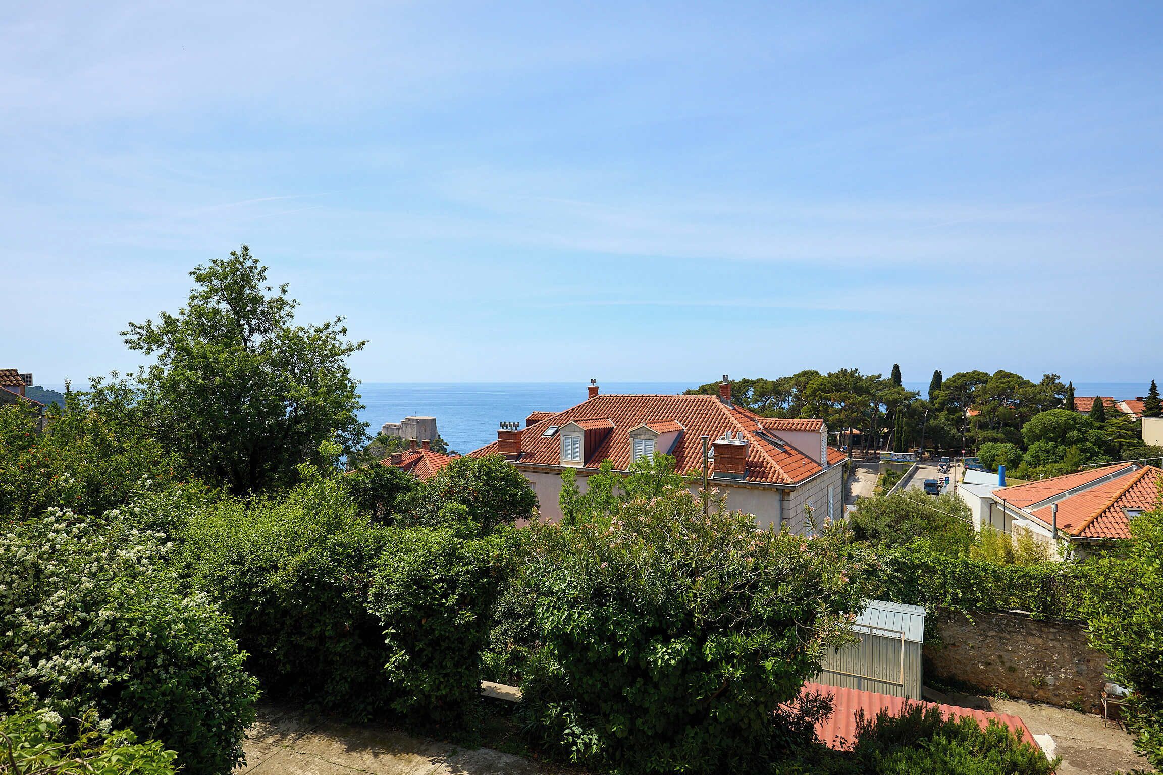 A coastal residential area with houses, dense greenery, and a clear view of the sea.