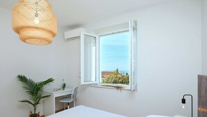 A bedroom with a bed, a desk, a chair, a potted plant, and a window with an open view. - Evergreen Escape (Dubrovnik)