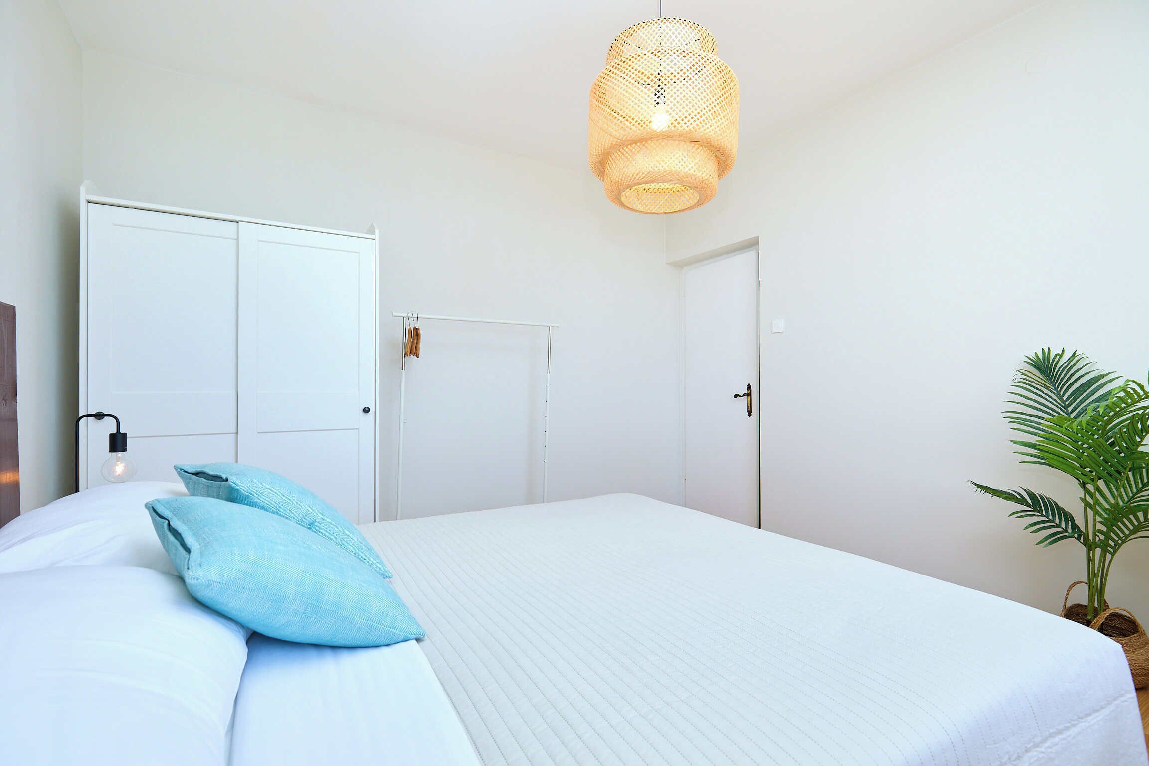 Un dormitorio con una cama grande, paredes blancas, una lámpara colgante y una planta en maceta.