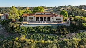 Una casa grande con piscina, rodeada de abundante vegetación y viñedos.