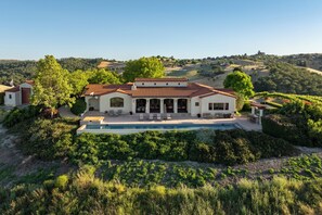 A large house with a swimming pool, surrounded by lush greenery and hills. - Private Pool + Spa | Templeton El Pomar District | Krisyn Vineyards (Templeton)