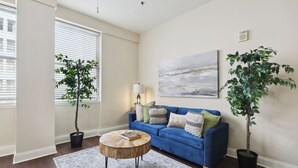 A living room with a blue sofa, two potted plants, a round coffee table, a rug, and a painting on the wall. - Suite Bleu |5 Min walk to Bourbon st| Rooftop Pool (New Orleans)