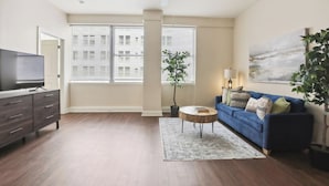 A living room with a TV, sofa, coffee table, and a painting on the wall. - Suite Bleu |5 Min walk to Bourbon st| Rooftop Pool (New Orleans)
