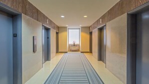 A hallway with two elevators, a central light source, and a patterned carpet. - Suite Bleu |5 Min walk to Bourbon st| Rooftop Pool (New Orleans)