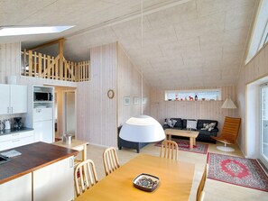 Cocina moderna con armarios blancos, microondas y cafetera. Hay un comedor con mesa y sillas de madera, y un sofá con alfombra roja.