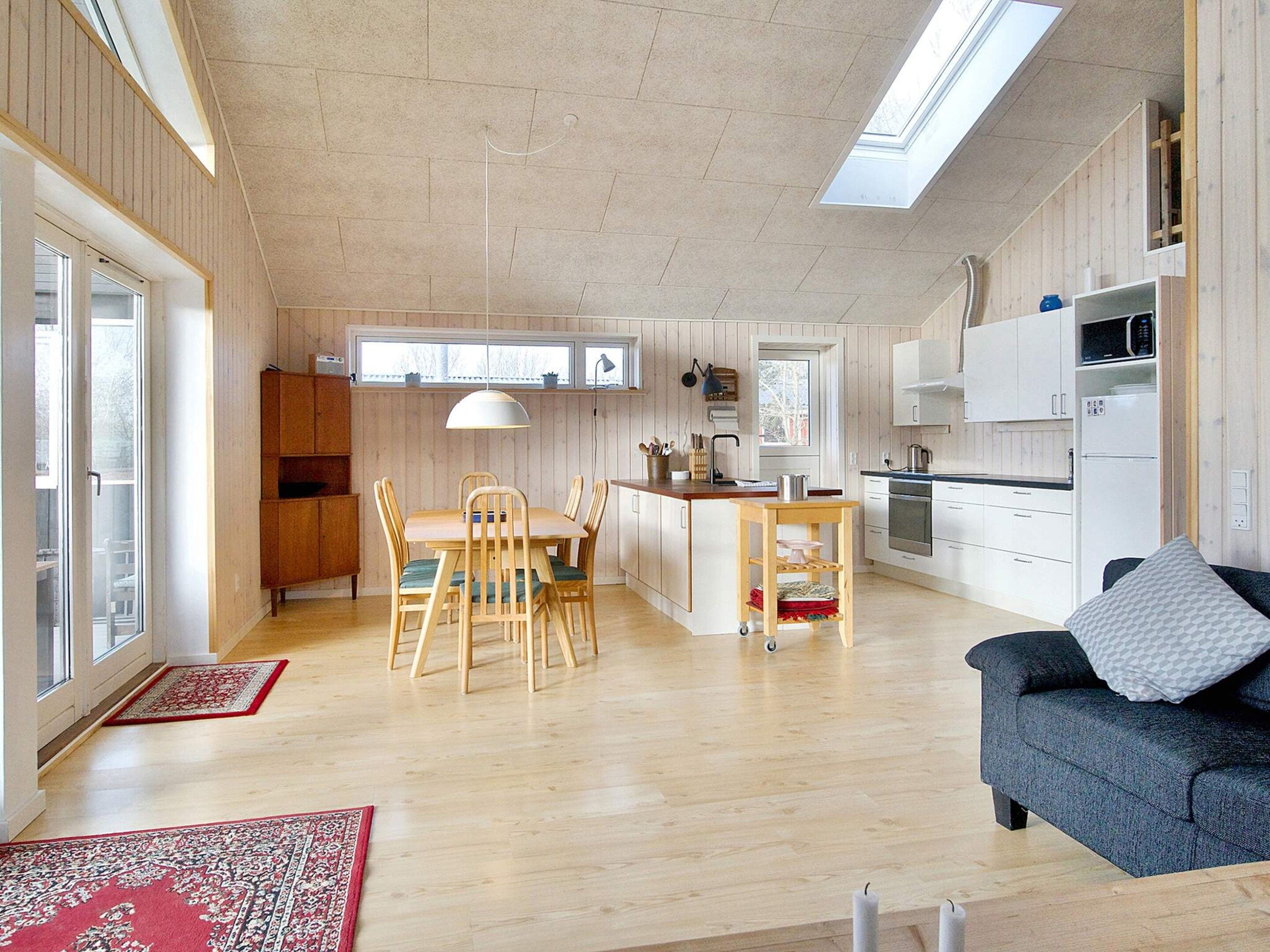 A modern kitchen with wooden cabinets, a dining area with a table and chairs, and a sofa in a living room.
