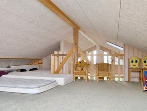A loft bedroom with a sloped ceiling, wooden beams, a bed, two wicker chairs, and a teddy bear. - 4 Star Holiday Home in Gorlev (Gørlev)